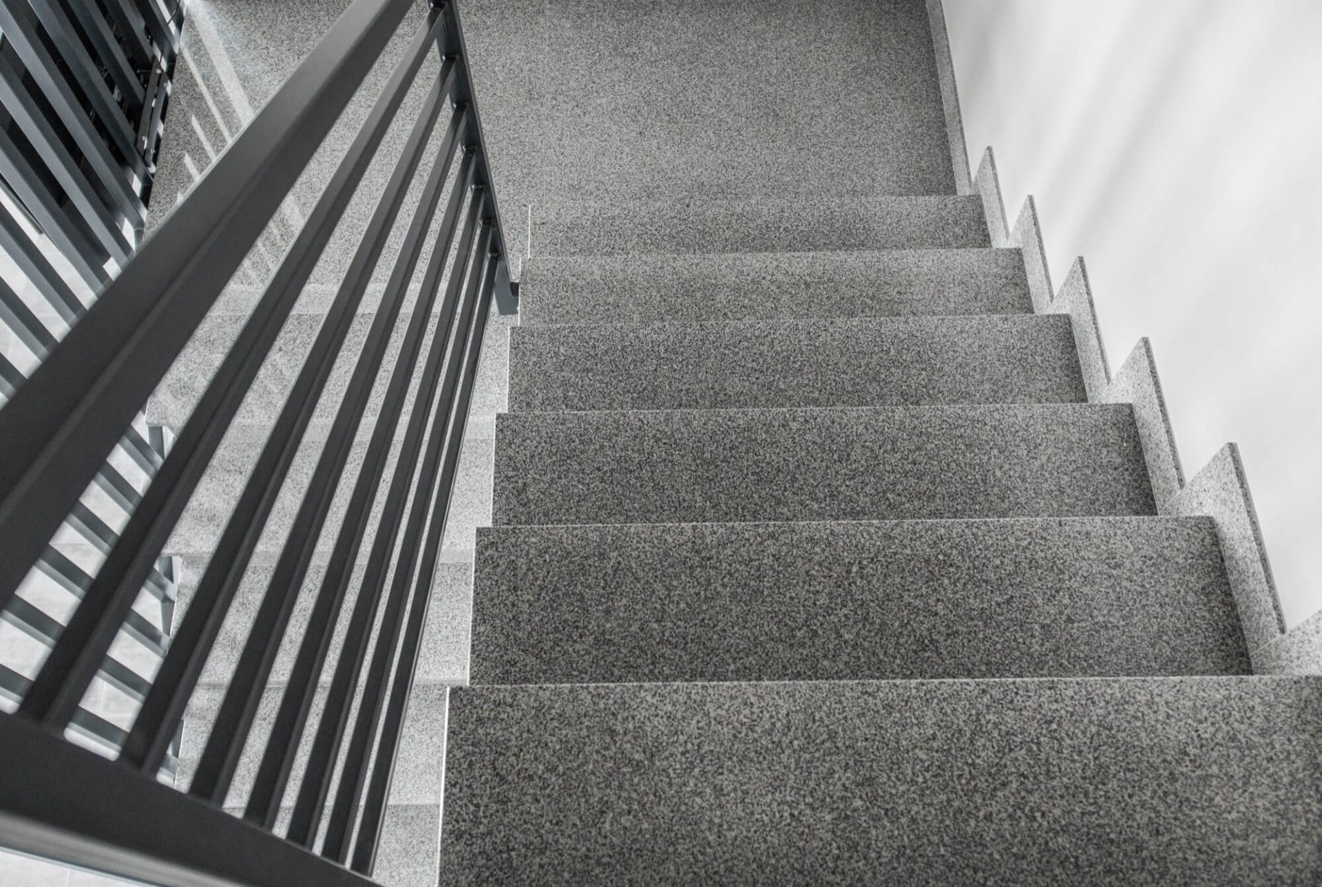 Ylhäältä päin kuvatut modernit harmaat betoniportaat mustalla metallikaiteella. Portaat ovat kivipintaiset ja luovat elegantin ilmeen.